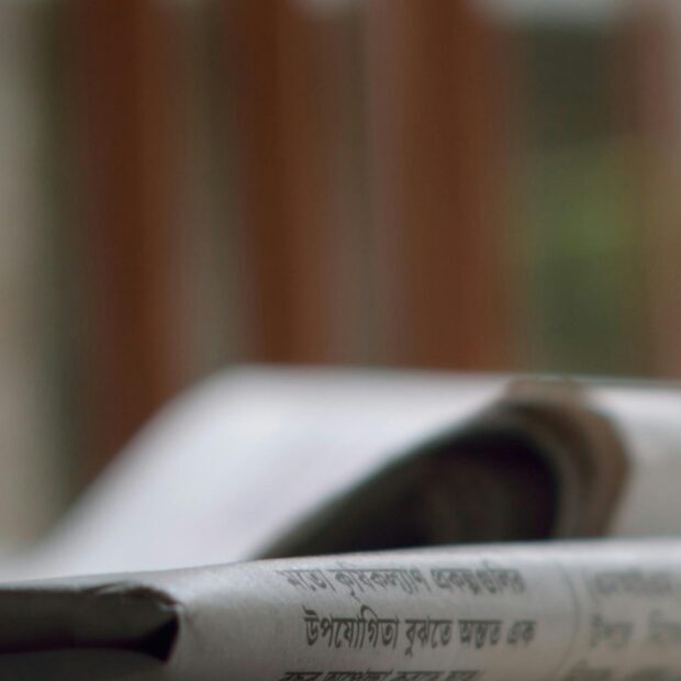 A close-up of a stack of newspapers resting on a desk, symbolizing information and media.